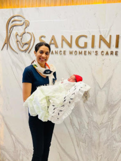 Woman holding a baby in front of a 'Sangini' sign